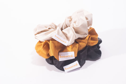 Three large scrunchies; one sand, one topaz, and one black with bounced logo